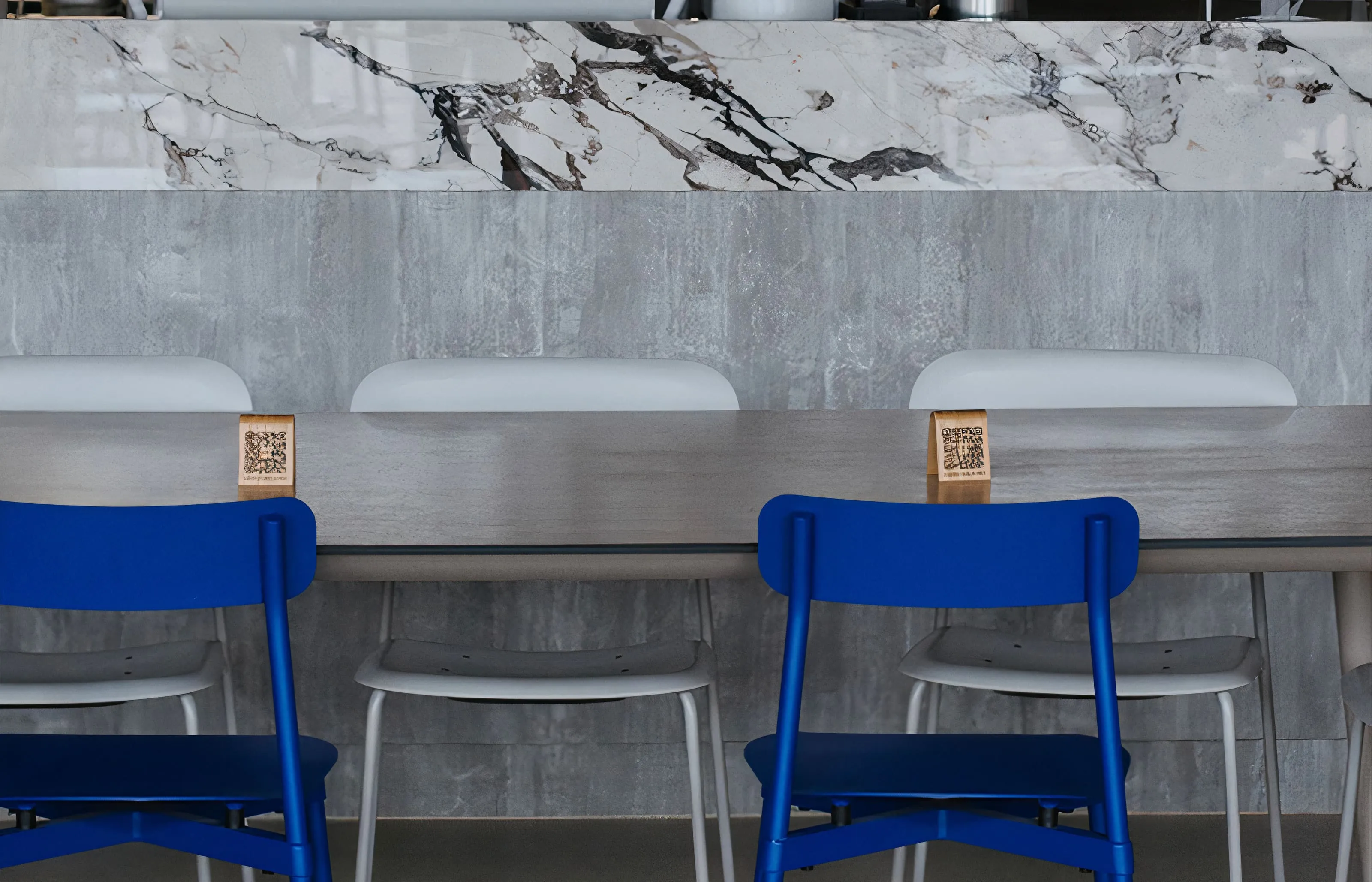 Inside BQ Canteen: blue chairs at a long concrete table under a marble wall
